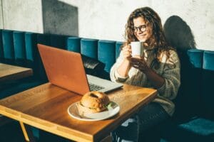 Young woman sitting at caffe, drinking coffee and working on laptop.